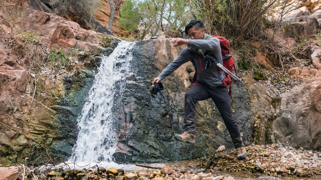 Rafael jumping over a stream with camera in hand.