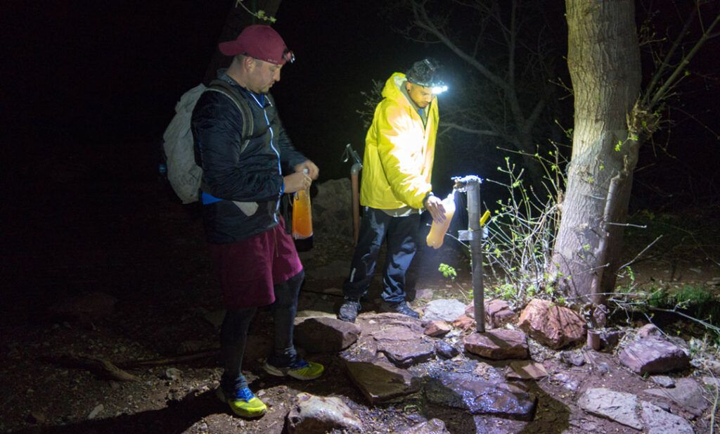 Hikers filling water bottles from a faucet at night.