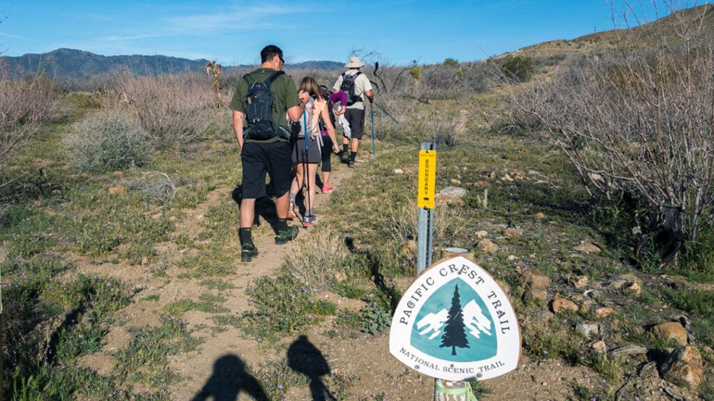A group of hikers hiking past the PCT sign to Grapevine Mountain.