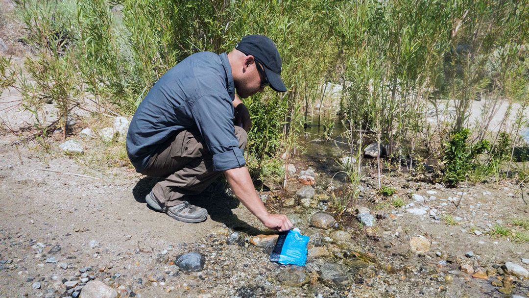 A hiker refills his water bottle from a small stream.