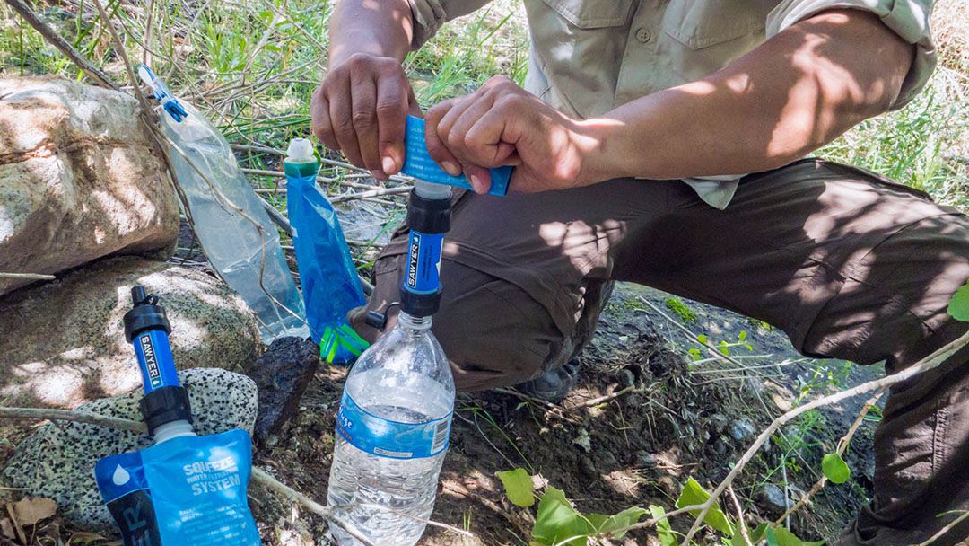 A hiker transfers water filtered from a stream to his water bottle.
