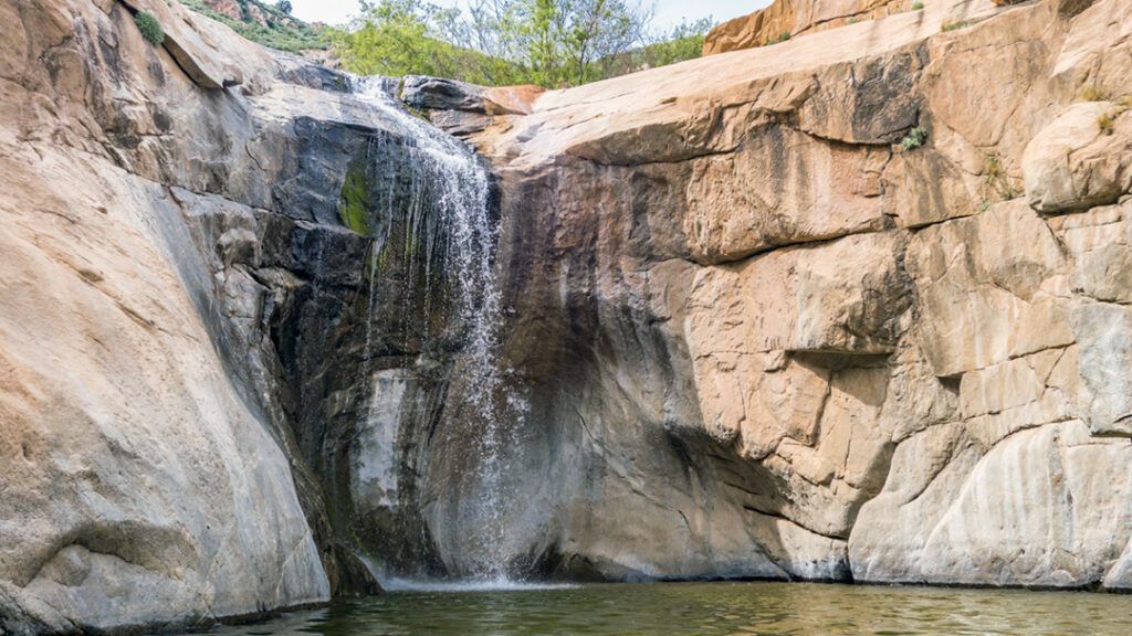 The third of three sisters falls from the trail flowing with water into a clear pool.